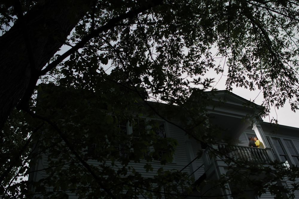 Two men in suits stand on a road. One has arms crossed, a yellow tie. The other is beside him, also in a suit, with dark sunglasses.