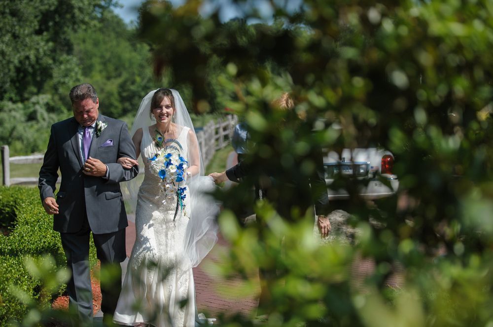 Bride and groom embrace outdoors, groom kisses bride's cheek. Black and white photo with blurred forest background.