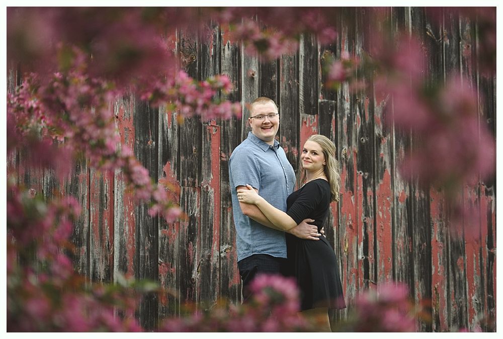 Bride and groom in wedding attire walking and kissing on a tree-lined road.