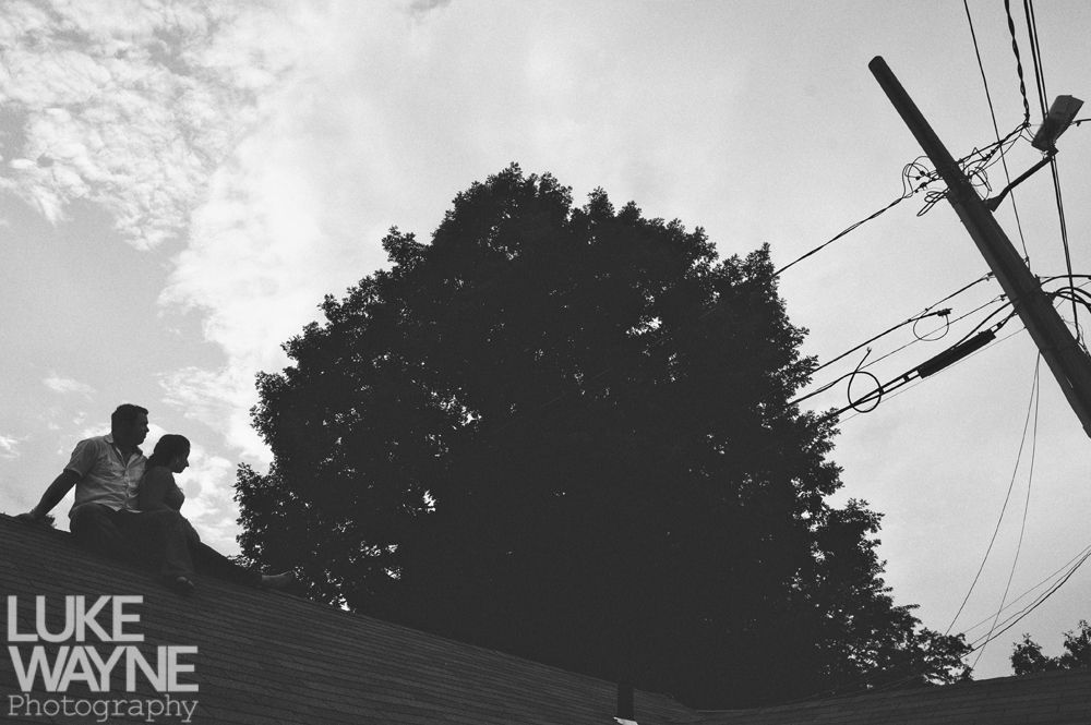 Couple silhouetted on a rooftop, large tree and telephone pole in the background, black and white.