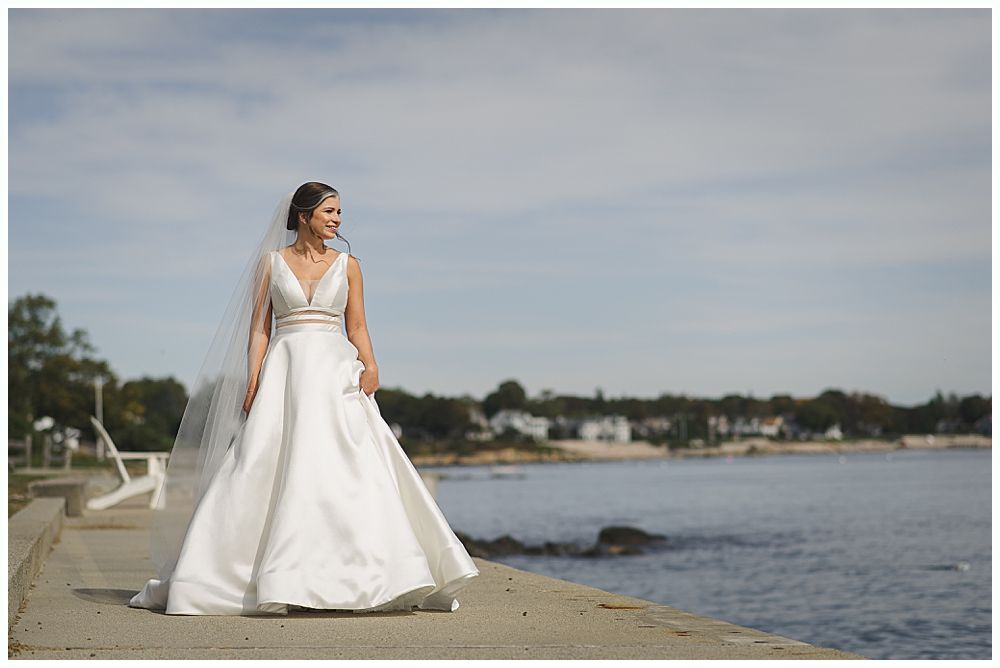 Groomsmen in dark suits pose on a grassy hillside under a cloudy sky.