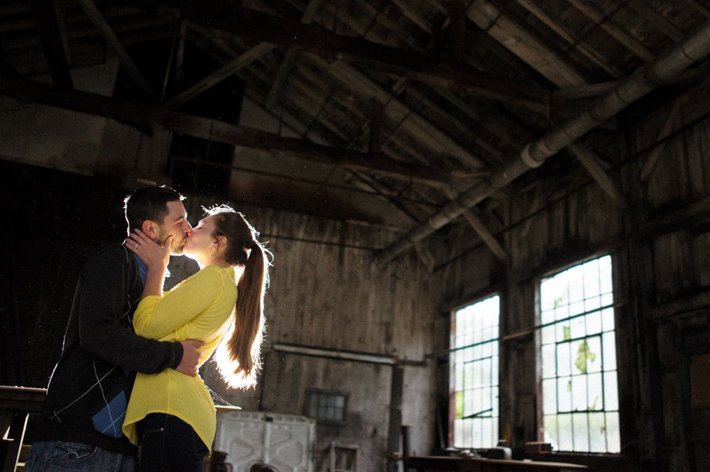 Bride and groom in wedding attire walking and kissing on a tree-lined road.