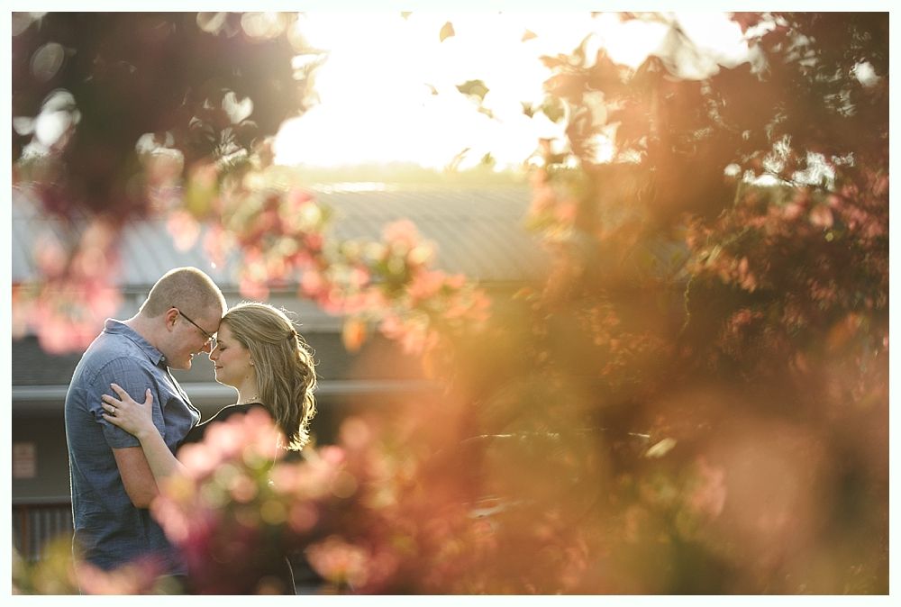 Bride and groom kissing amidst trees, holding bouquets. Black and white photo.