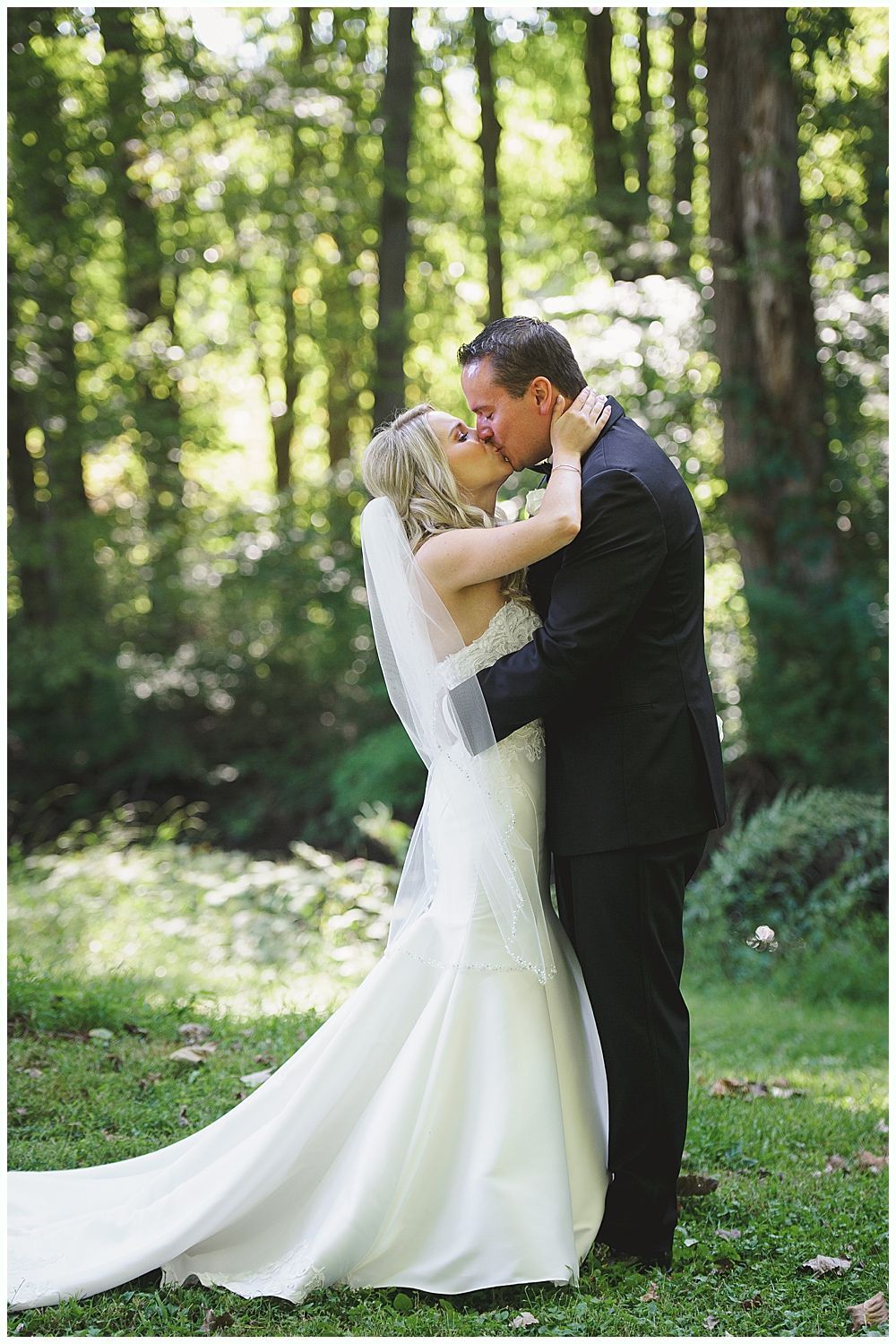 Groomsmen in dark suits pose on a grassy hillside under a cloudy sky.