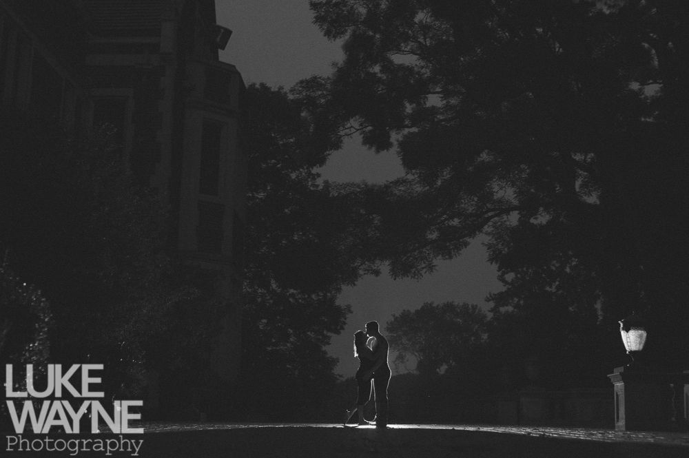 Couple kissing silhouetted against a building and trees at night.
