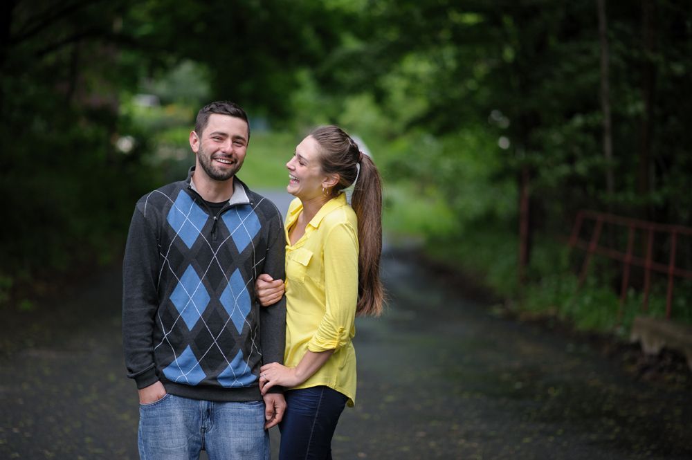 Bride and groom kissing amidst trees, holding bouquets. Black and white photo.