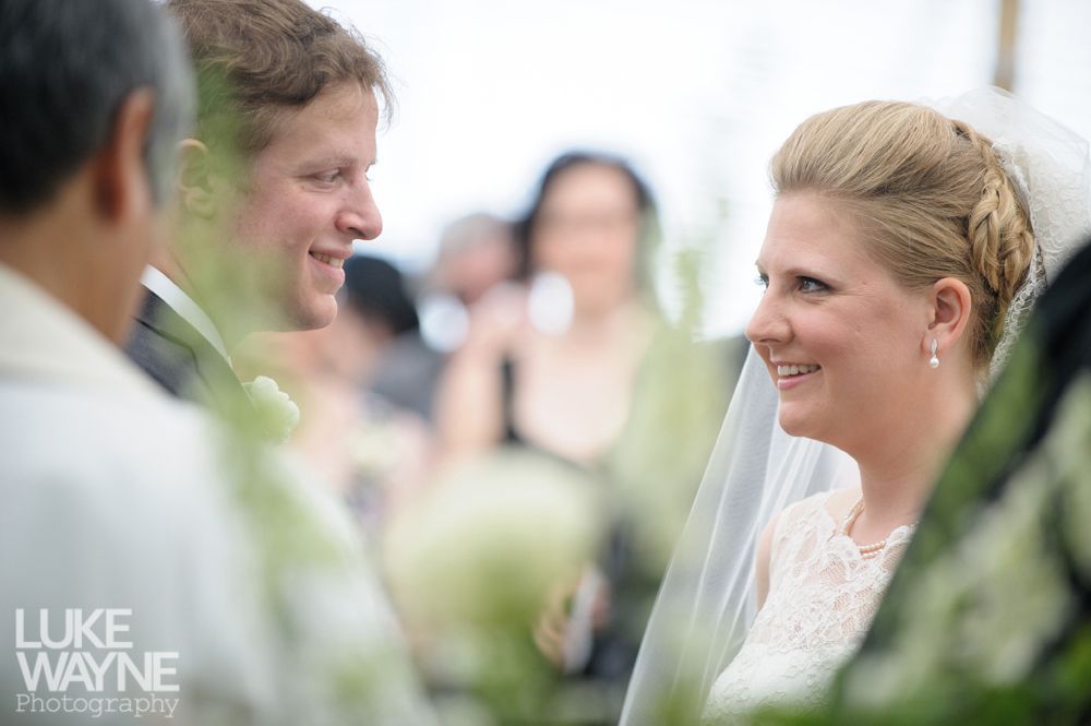 Bride and groom smiling at each other during a wedding ceremony. White dress, veil, and soft focus background.