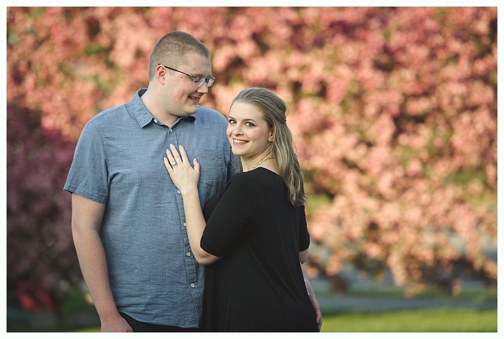 Bride walks down a path with two men, holding a yellow bouquet. Fountain and building in the background.