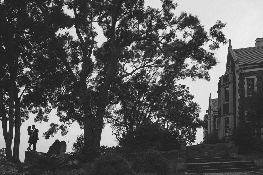 Black and white photo of a building next to trees, with a statue and steps in the foreground.