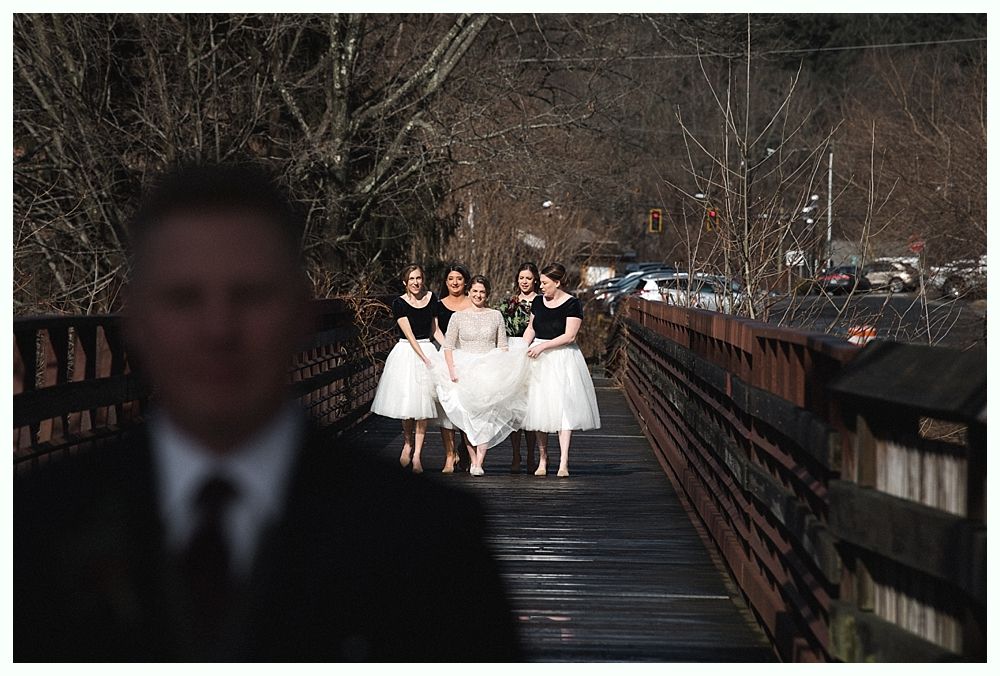 Wedding ceremony: Bride and groom walking toward barn, bridesmaids in red dresses holding bouquets.