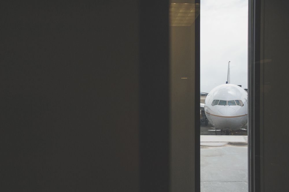 Bride and groom under umbrella, backlit by light. Mountain backdrop in dark, black and white photo.