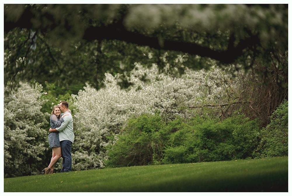 Bride walking with her father down an outdoor aisle; fall trees and guests in background.