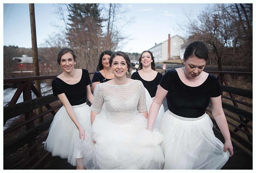 Bride walking with her father down an outdoor aisle; fall trees and guests in background.