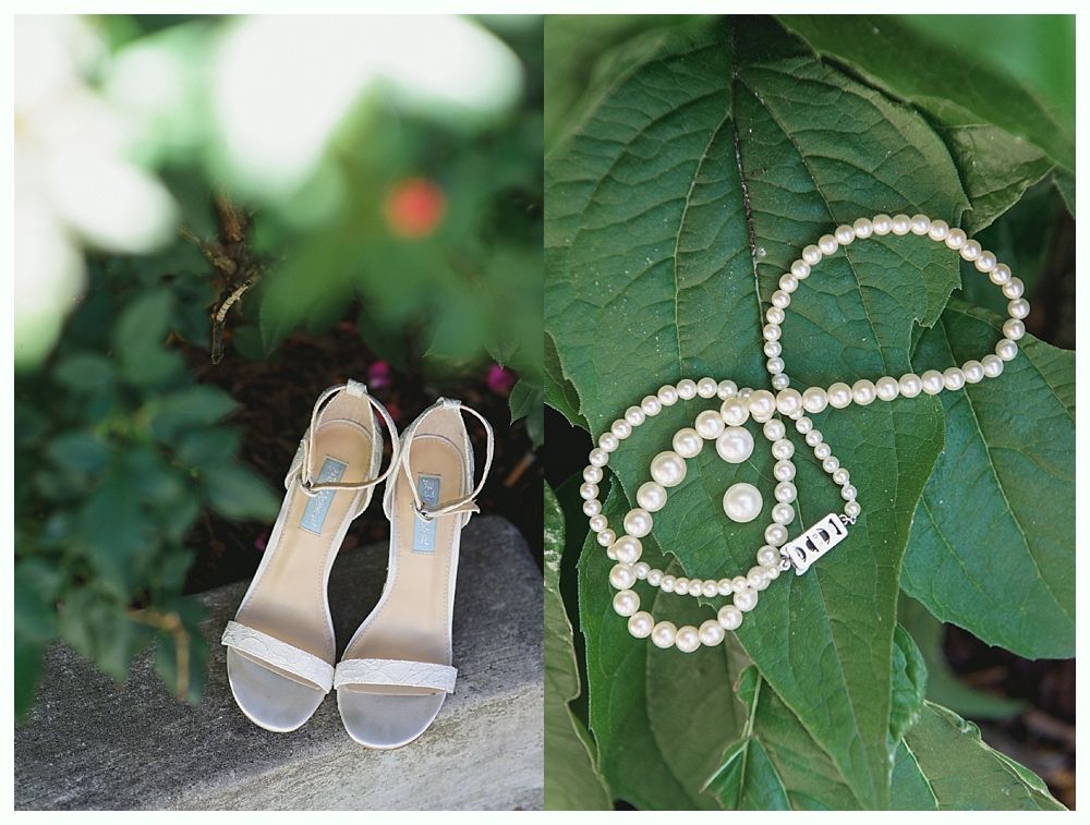 Sandals on a rock, next to a pearl necklace and earrings on a green leaf.