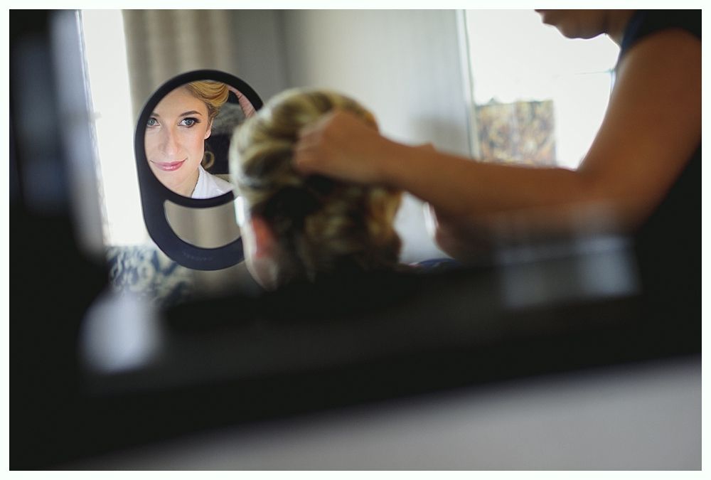 Woman reflected in mirror as hairstylist works on her updo.