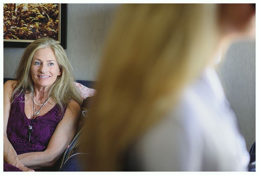 Woman in purple dress smiles, seated indoors, looking towards another person.