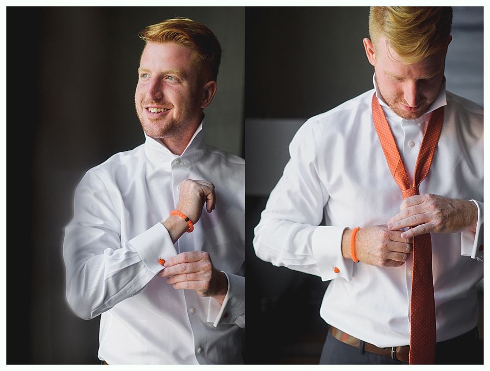 Man adjusting his cufflinks and tie in a bright room. He wears a white shirt and orange accessories.