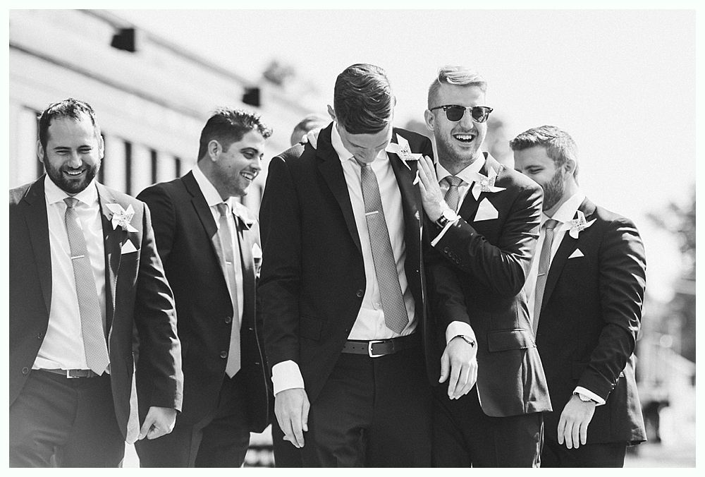 Men in suits smile and laugh outdoors.
