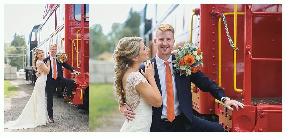 A bride and groom pose by a red train. The couple embrace and smile.