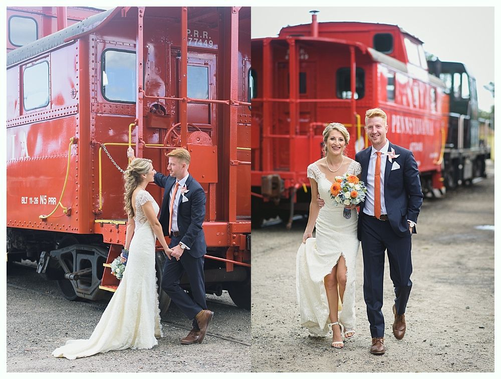 Bride and groom pose by red train cars, holding hands.