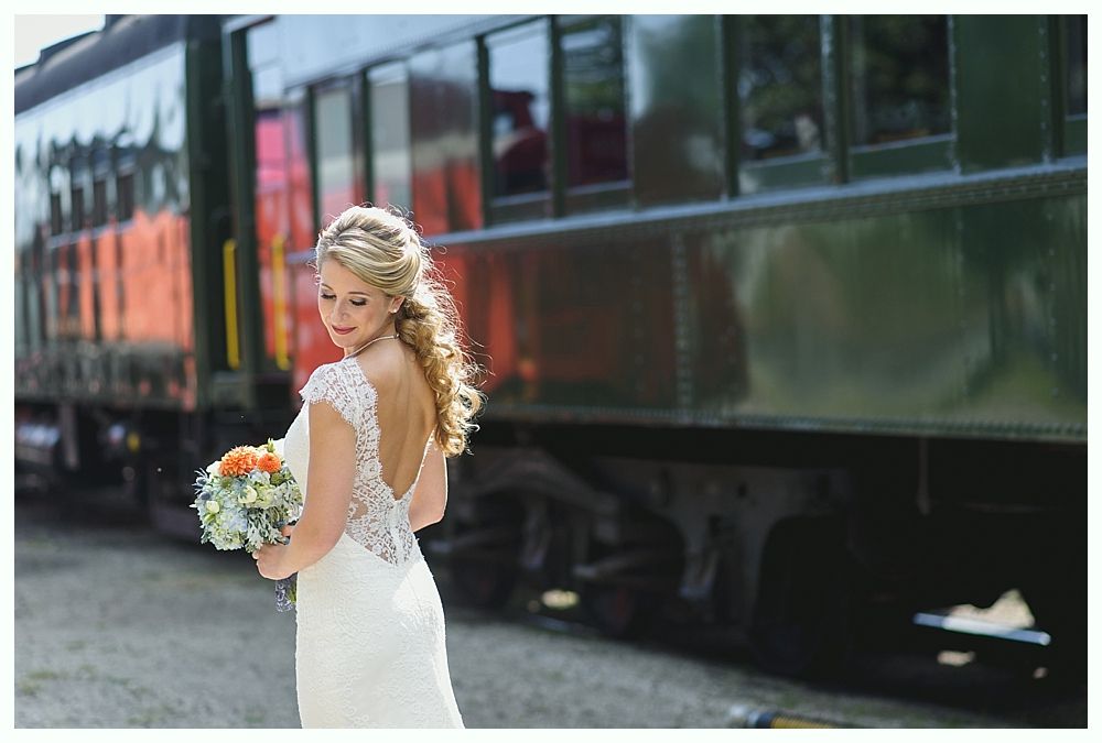 Bride in wedding dress, holding bouquet, standing in front of a train.
