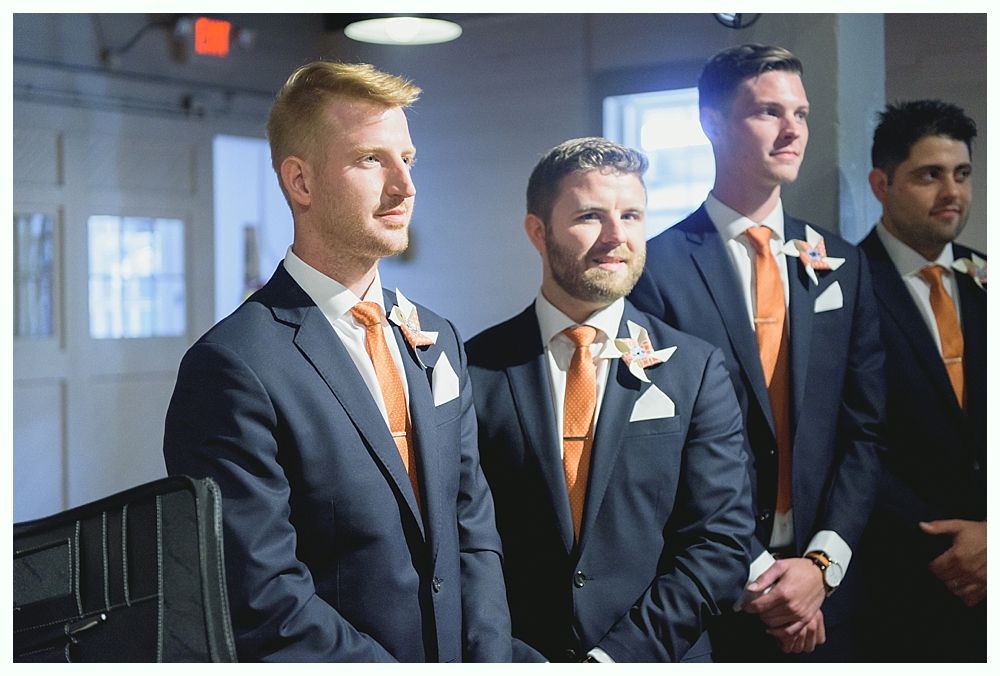 Four men in suits with orange ties, posing inside a building.