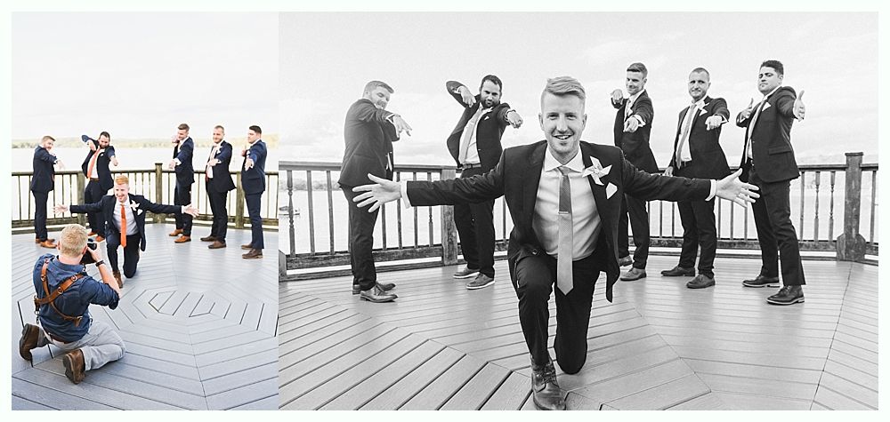 Groomsmen on a deck posing for a photo. One kneels with arms outstretched; others point or act like they're taking photos.