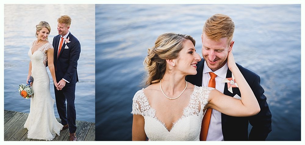 Wedding couple smiling, posing on a dock by water. Man in a suit, woman in a white dress with bouquet.