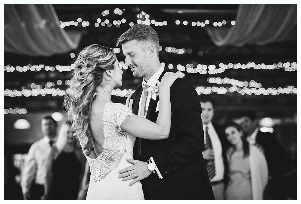 Bride and groom dance at a wedding reception, looking at each other, in black and white.