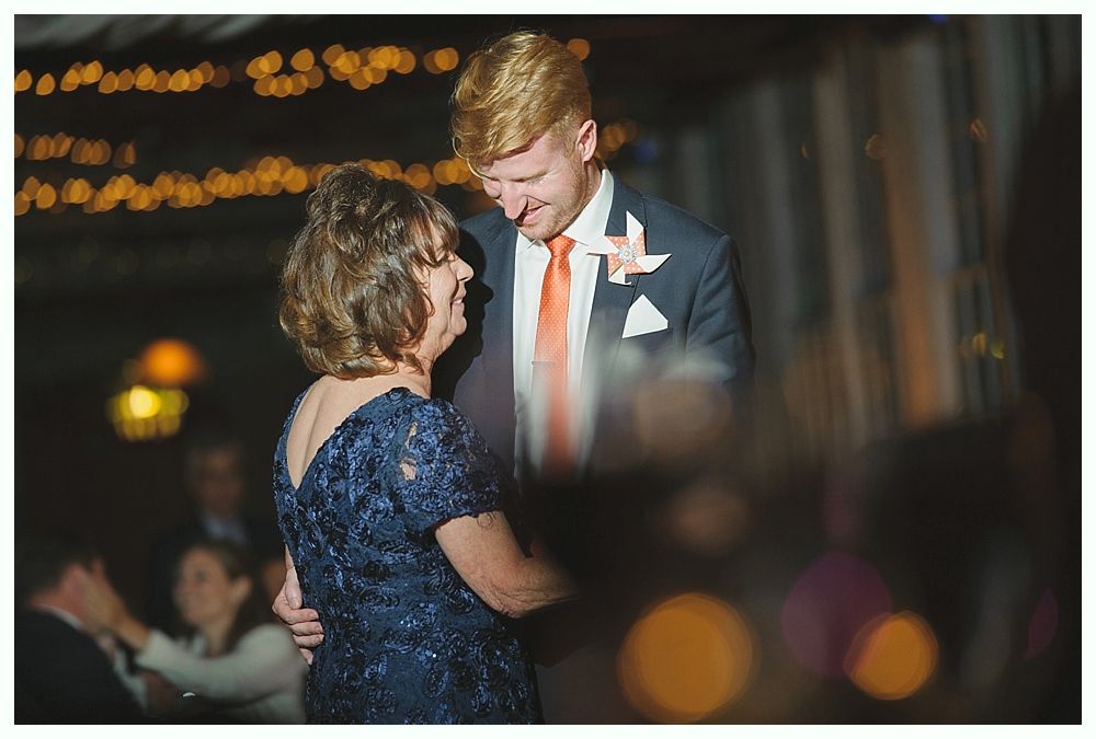 Man dances with woman at a wedding. Man wears a suit with an orange tie, woman in a navy dress.