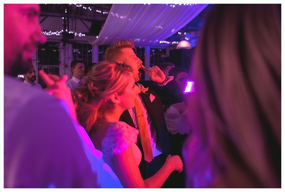 Couple dancing and singing at a wedding reception with purple and pink lighting.