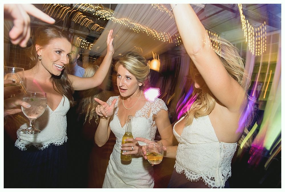 People dancing at a wedding reception, dressed in white tops and dresses, holding drinks.