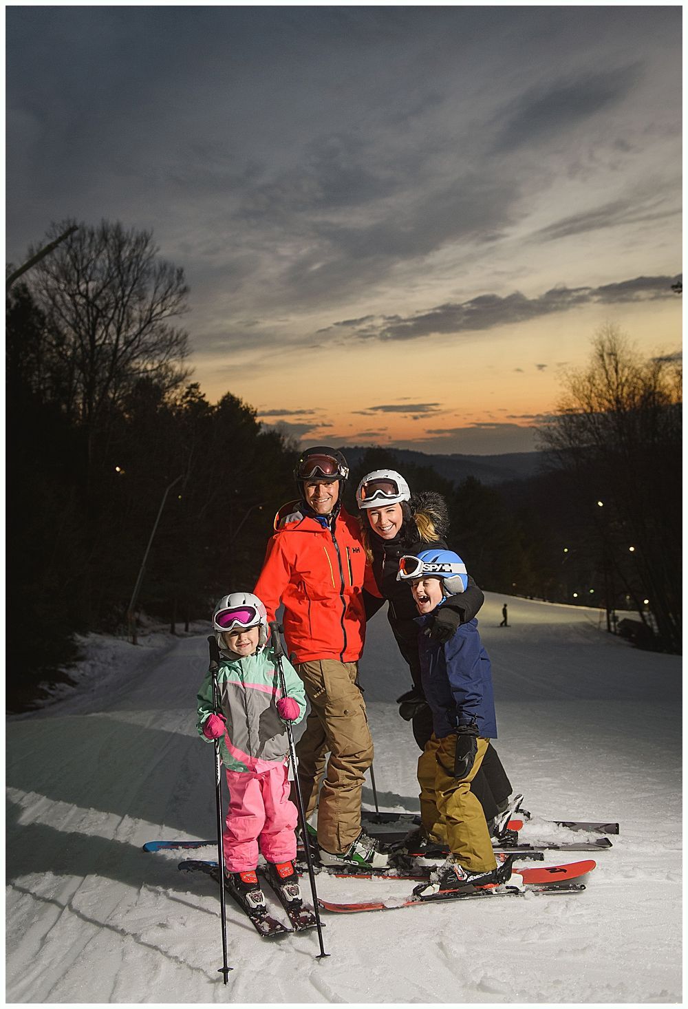 Family in ski gear poses on a snowy slope at sunset.