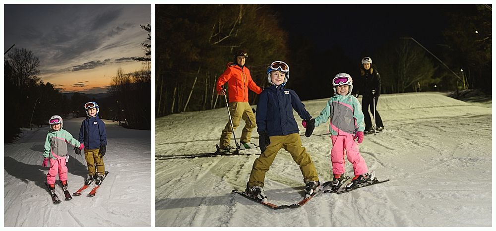 Two children skiing at dusk, holding hands. They wear helmets and colorful ski clothes.