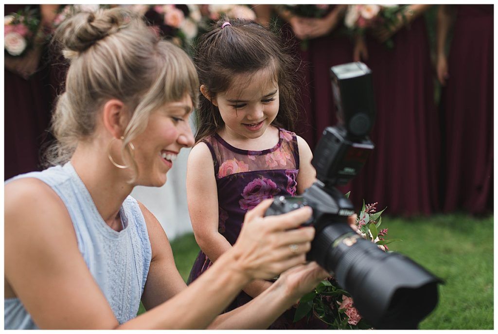Woman showing a young child how to use a camera outdoors, smiling.