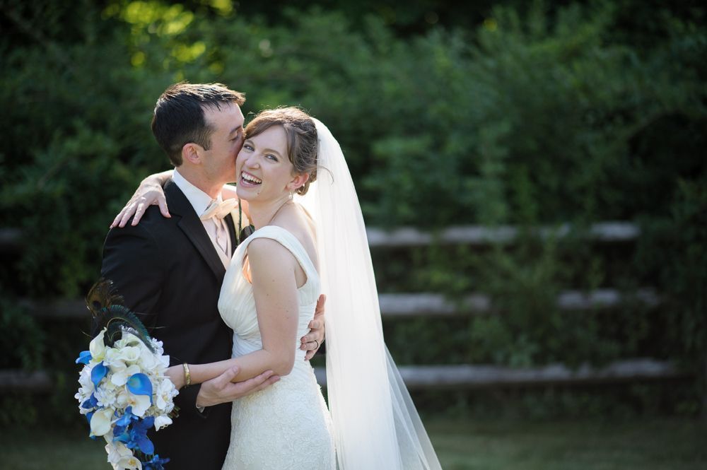 Newlyweds walk down aisle holding hands, sunflowers, gazebo in background.