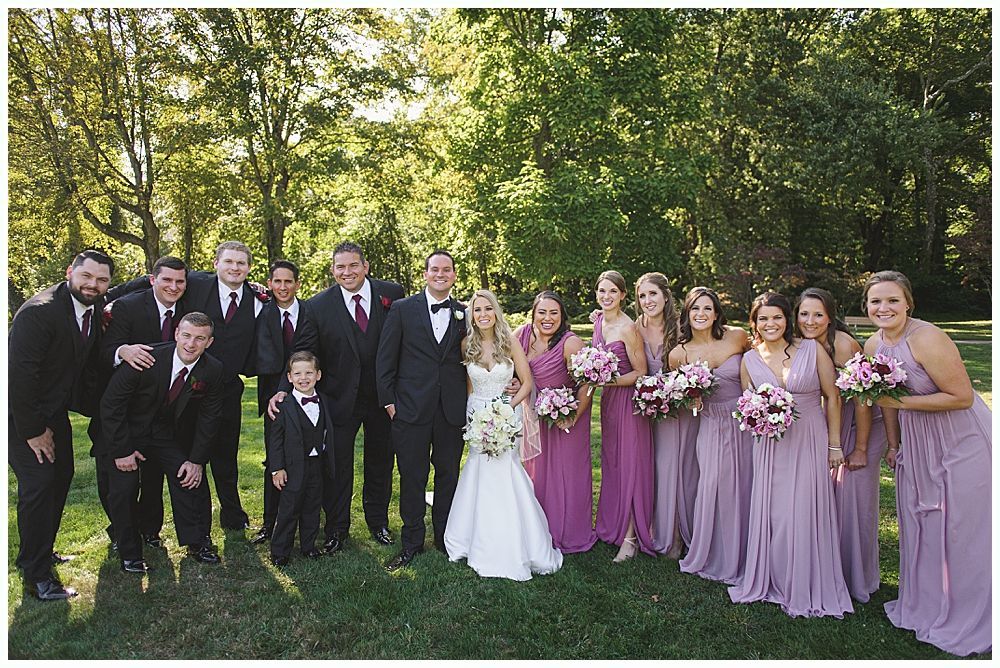 Bride walking with her father down an outdoor aisle; fall trees and guests in background.