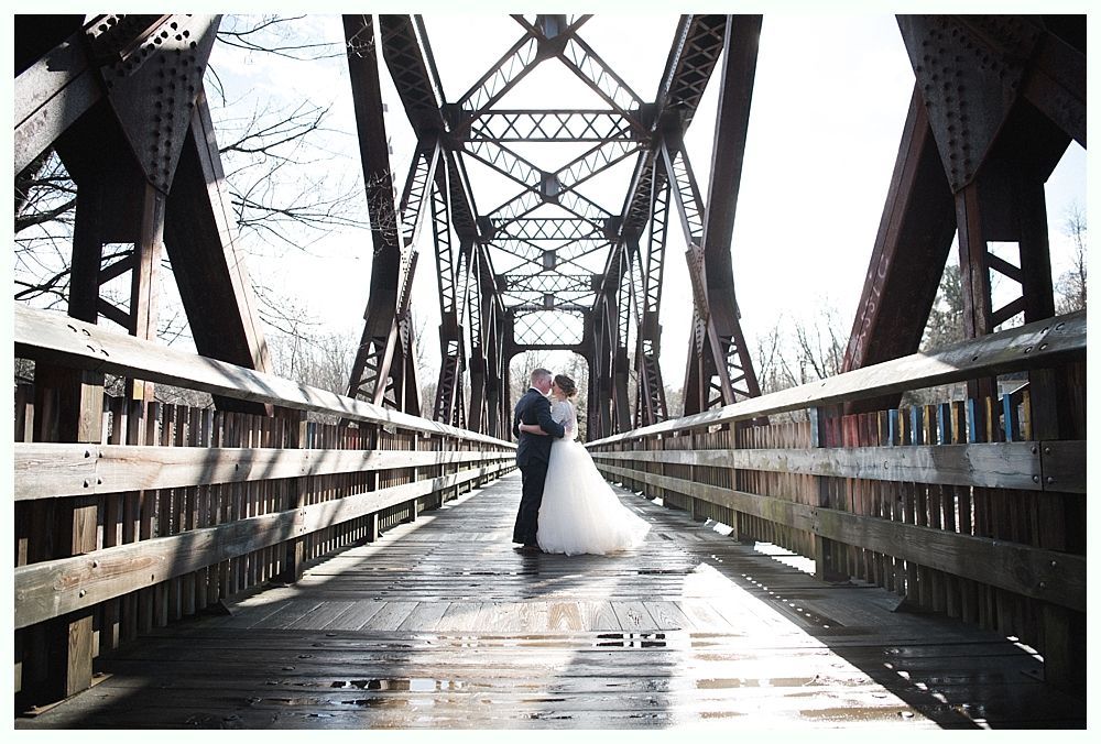 Bride hugging a man near outdoor wedding seating. People watch. The bride wears a white dress and veil.
