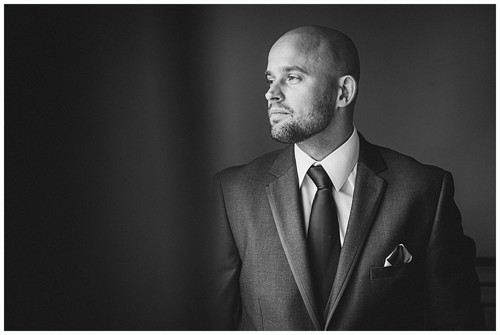 Wedding ceremony with groom and groomsmen smiling, floral arch in background.