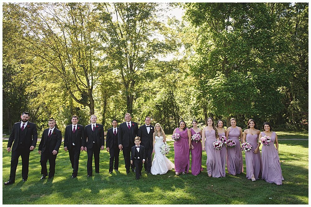 Wedding ceremony with groom and groomsmen smiling, floral arch in background.