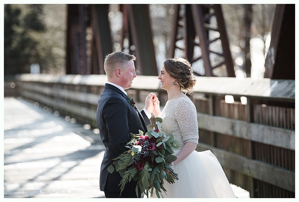 Couple embracing, noses touching, looking at each other. Snowy outdoor setting. Woman's hand with engagement ring visible.