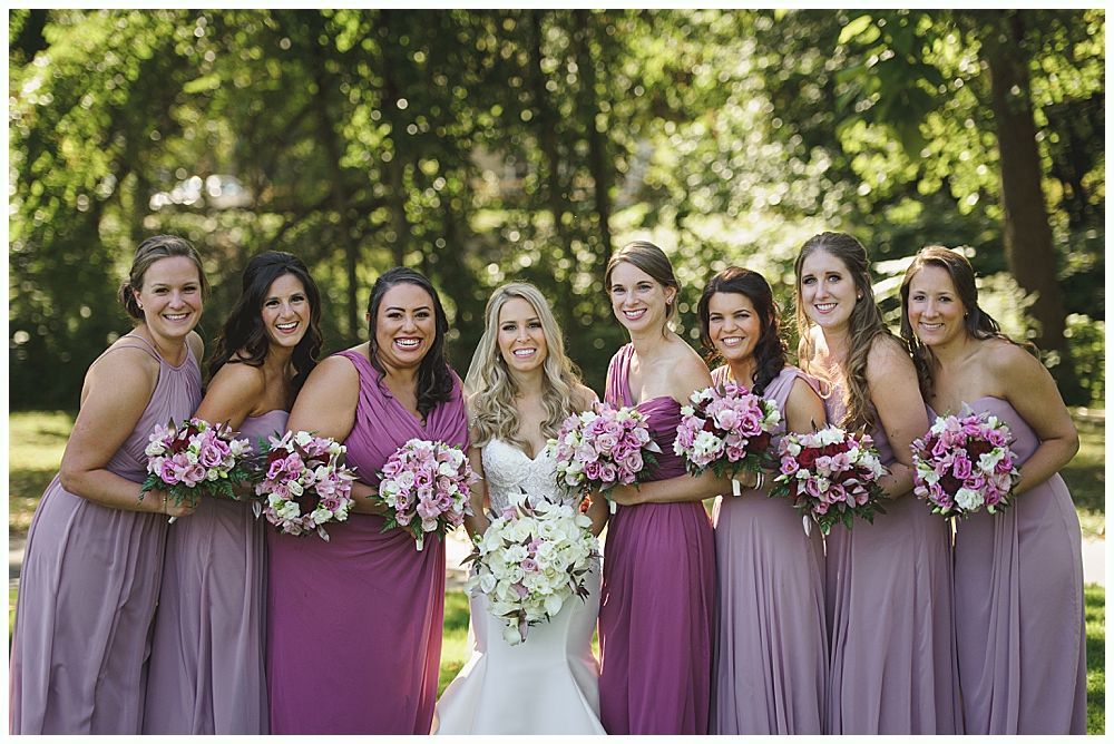 Bride hugging a man near outdoor wedding seating. People watch. The bride wears a white dress and veil.