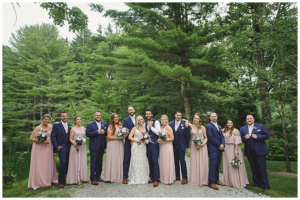Wedding ceremony. Guests seated, smiling. Groom facing officiant. Bride in white dress. Outdoors, sunny day.