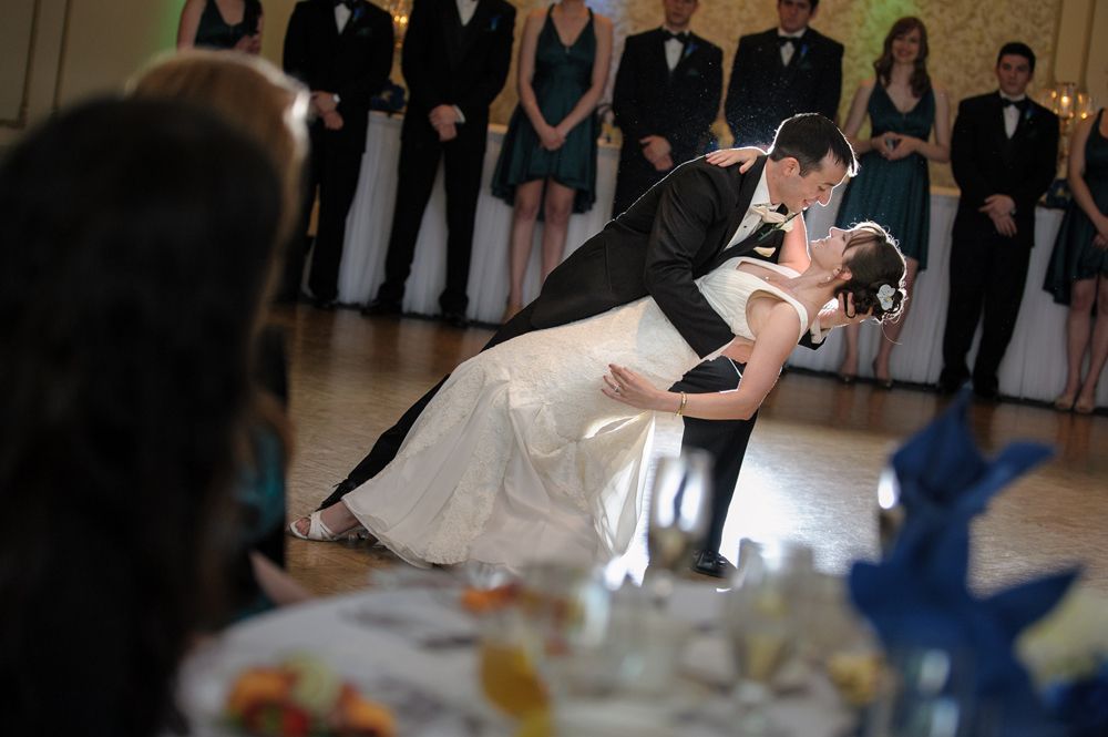 Bride and groom embrace, lit by spotlight against dark night sky and hillside.