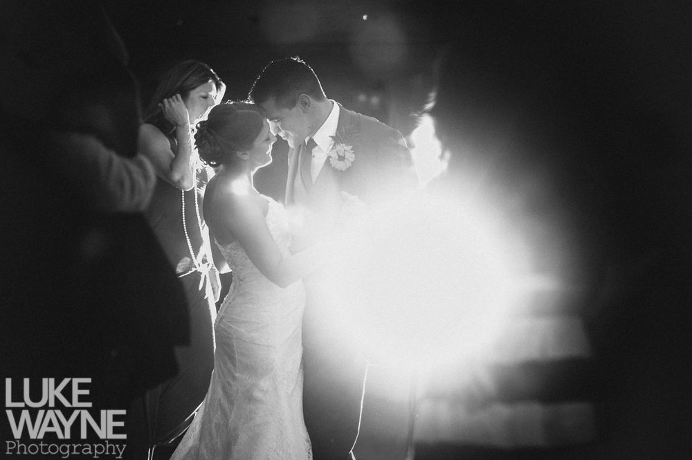 Wedding couple embraces, lit by bright flash. Stairs in background. Black and white.