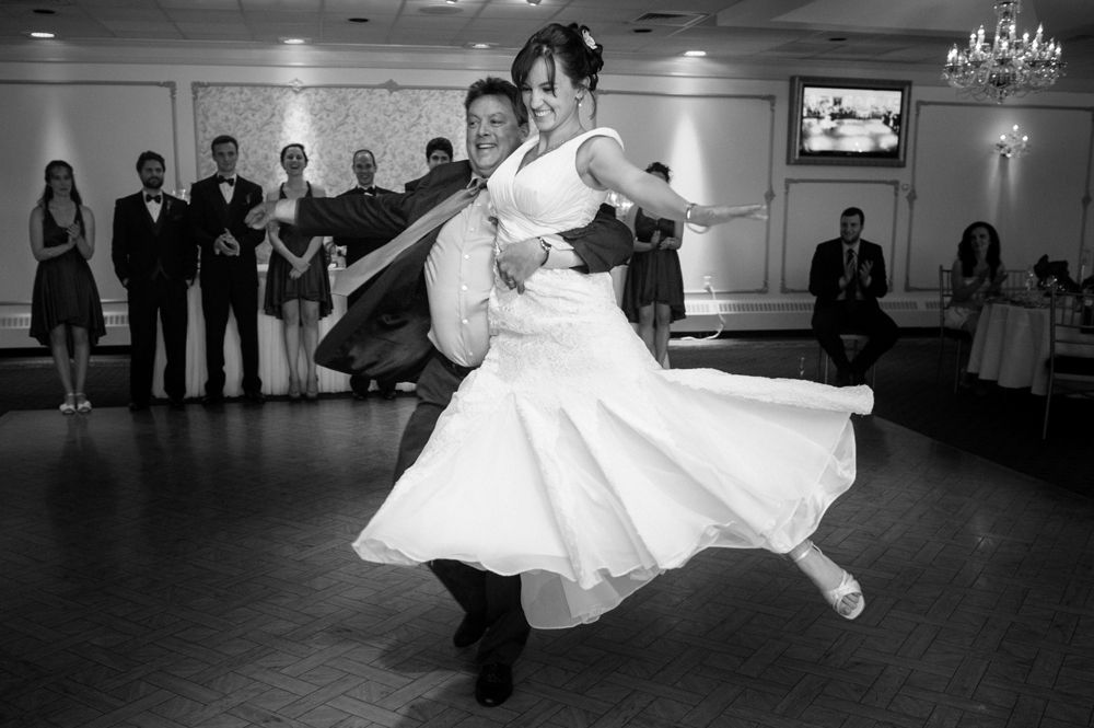 Bride and groom embracing, silhouetted under a large tree, in black and white.