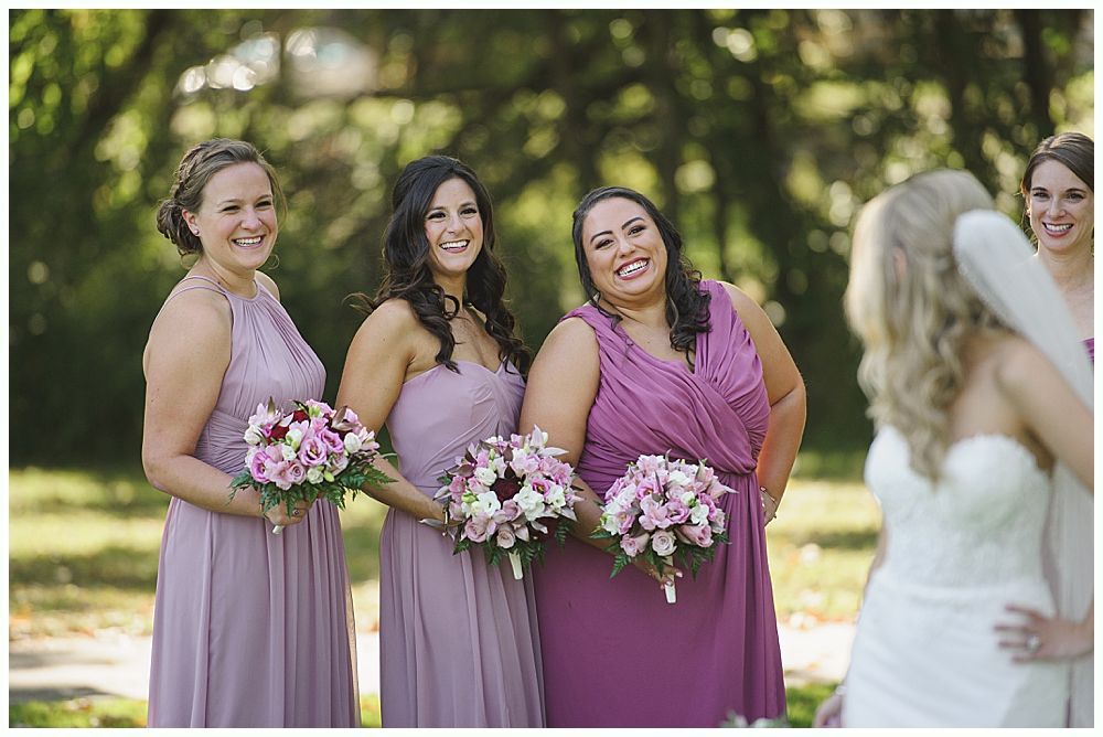 Wedding ceremony. Guests seated, smiling. Groom facing officiant. Bride in white dress. Outdoors, sunny day.