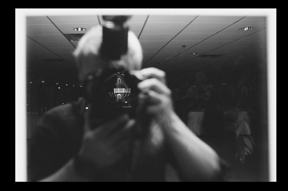 Person taking photo in mirror, indoors; black and white.