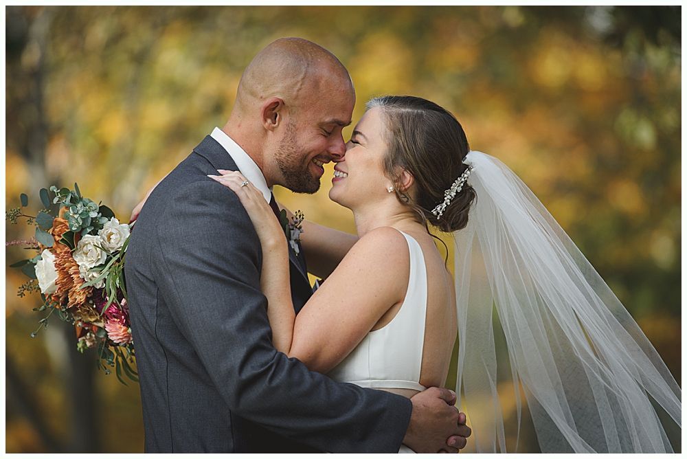 Bride smiles at the altar during a ceremony. Groomsmen in suits partially block view. Outdoor setting.