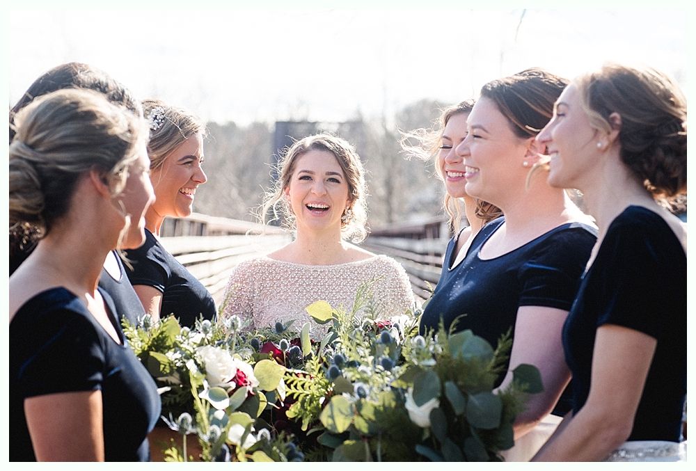 Wedding ceremony outdoors by a lake with a couple, wedding party, and guests under a cloudy sky.